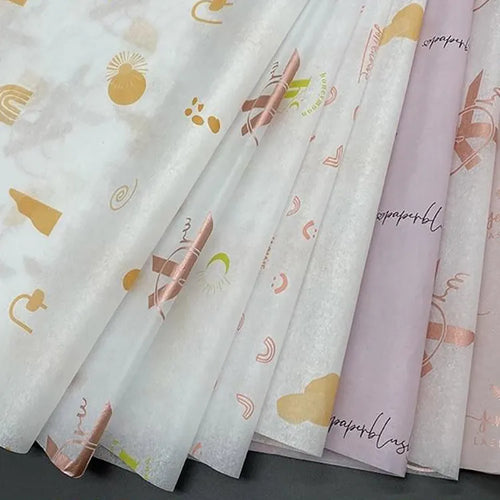 Overlapping white and pale pink tissue paper sheets printed with gold and pink decorative patterns