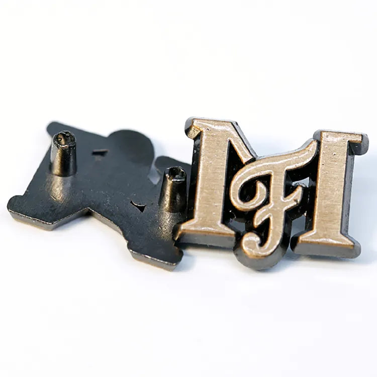 Front and back view of custom antique metal logo tag showing mounting posts for clothing and leather goods