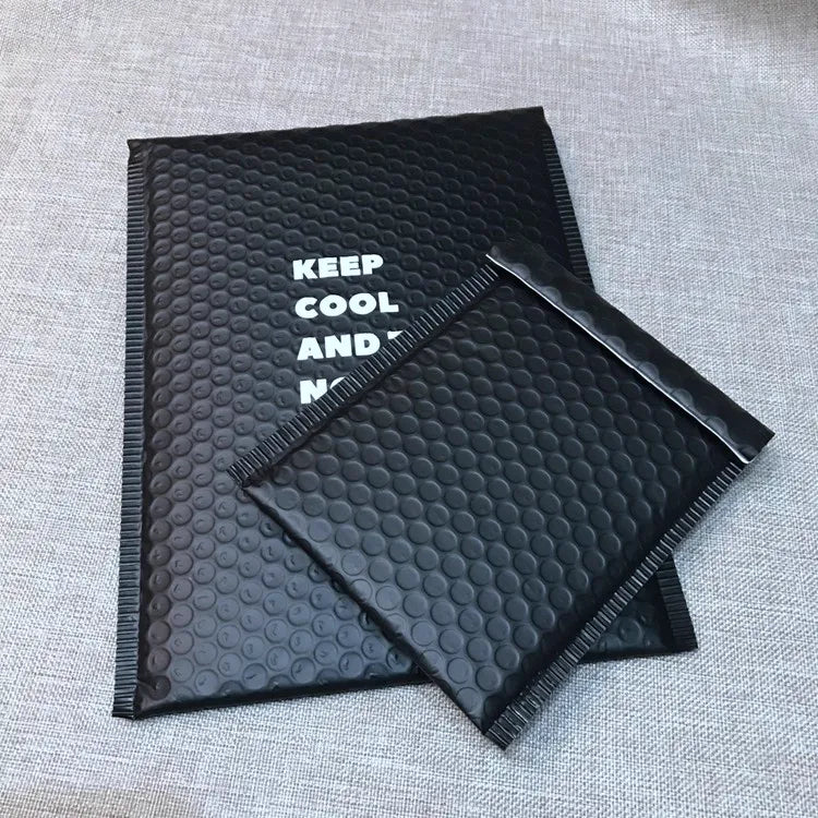 Two black bubble mailers with white printed lettering on a textured surface