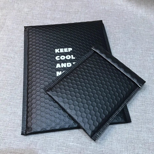 Two black bubble mailers with white printed lettering on a textured surface