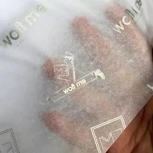 Translucent white wrapping tissue paper with silver-tone logos shown over an open hand