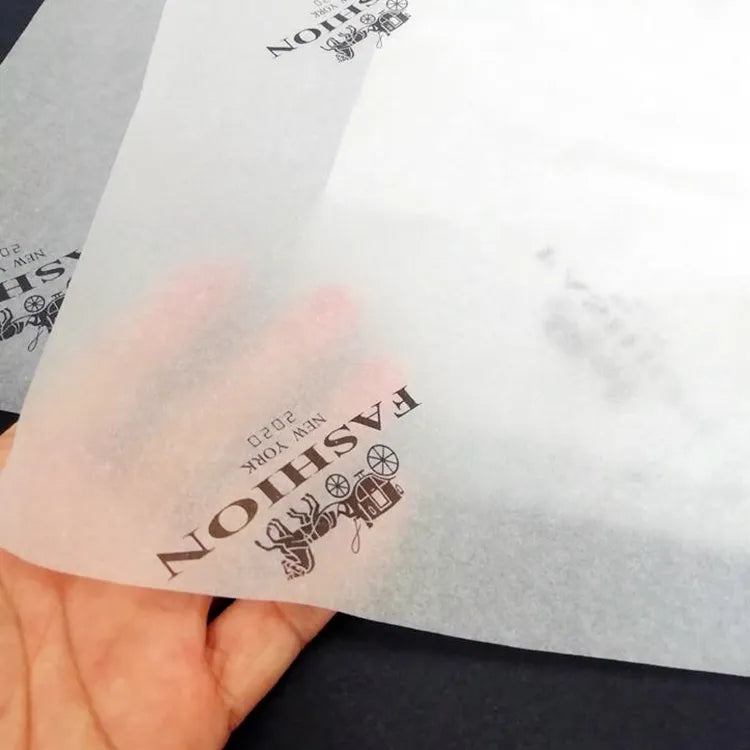 Hand holding translucent white tissue paper printed with a black fashion logo