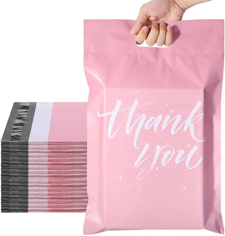 Hand holding a pink die-cut handle mailer bag with white Thank You lettering beside a stack of matching bags with black adhesive flaps