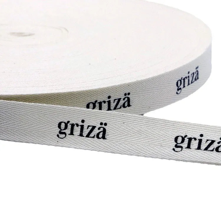 White herringbone cotton twill tape roll printed with black brand lettering for clothing labels