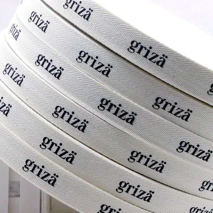 Neatly wound layers of white herringbone cotton tape printed with repeating brand name typography