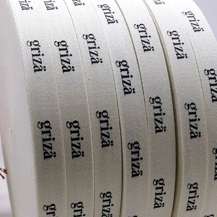 Side-by-side rolls of white herringbone cotton tape showcasing sharp repeating printed brand logos