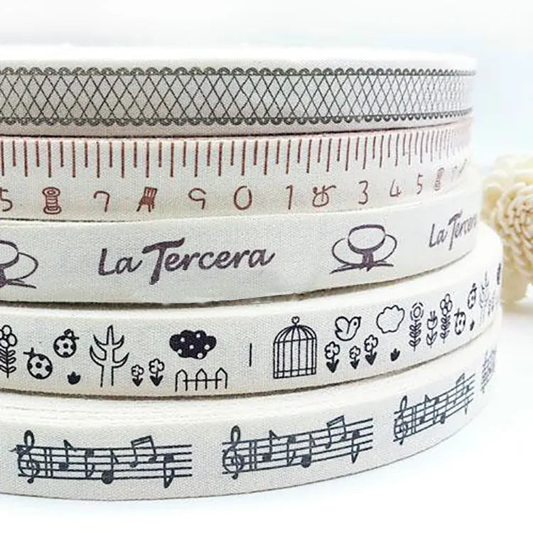 Stacked rolls of cream cotton ribbon printed with assorted decorative illustrations and text