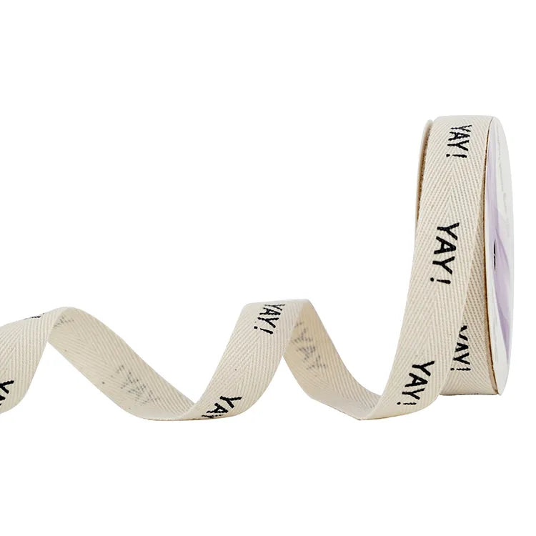 Cream herringbone cotton ribbon spool with repeating black printed lettering for hang tag ties