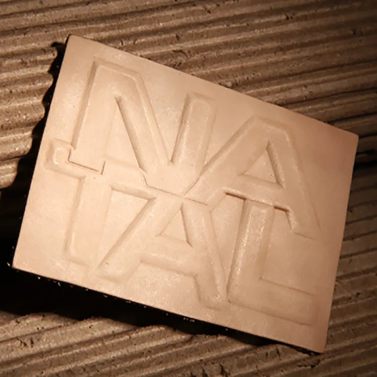 Natural off-white thick raw leather patch with deep debossed large geometric NATAL lettering across the entire surface