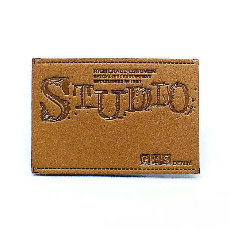 Tan leather patch with debossed vintage Studio wordmark, denim specifications, and precision perimeter stitching for jeans waistband