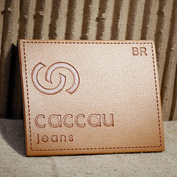 Textured pebble-grain tan PU leather patch with debossed spiral logo and caccau jeans lettering, featuring clean rectangular border stitching