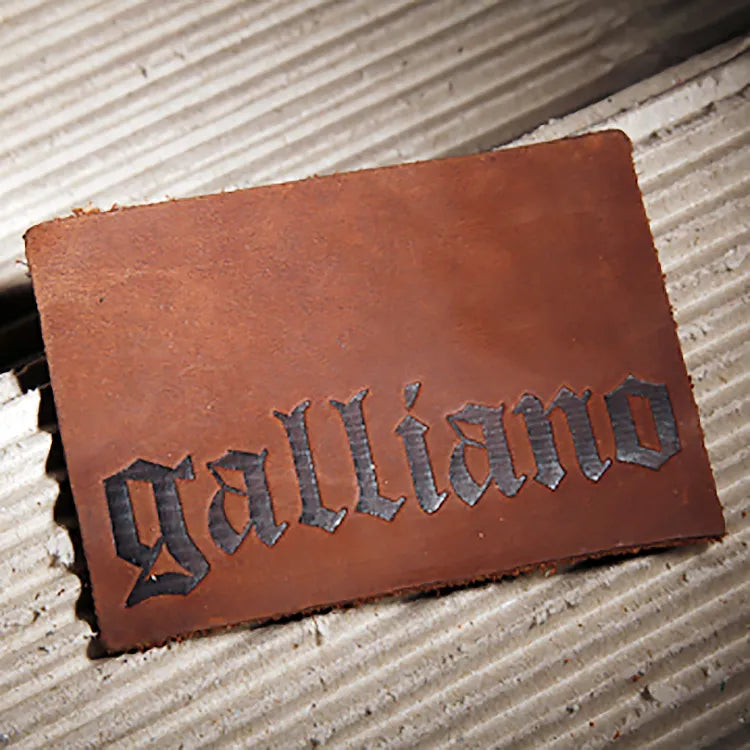 Rustic pull-up brown leather patch with raw unfinished edges and debossed Galliano gothic blackletter branding for vintage denim