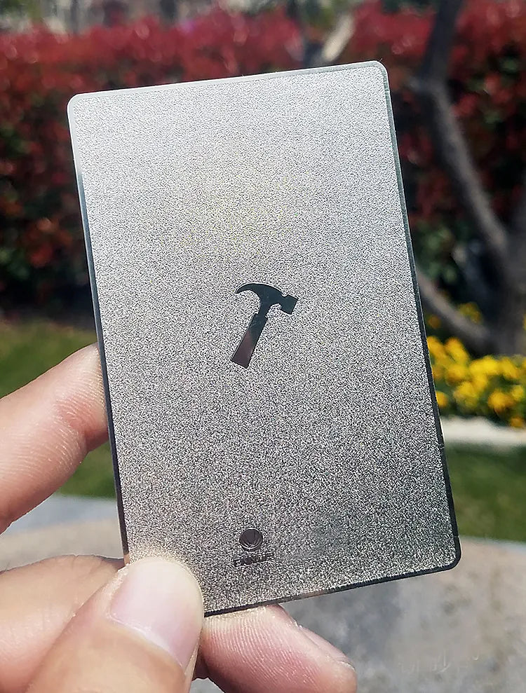 Silver-tone metal business card with a dark hammer symbol held outdoors