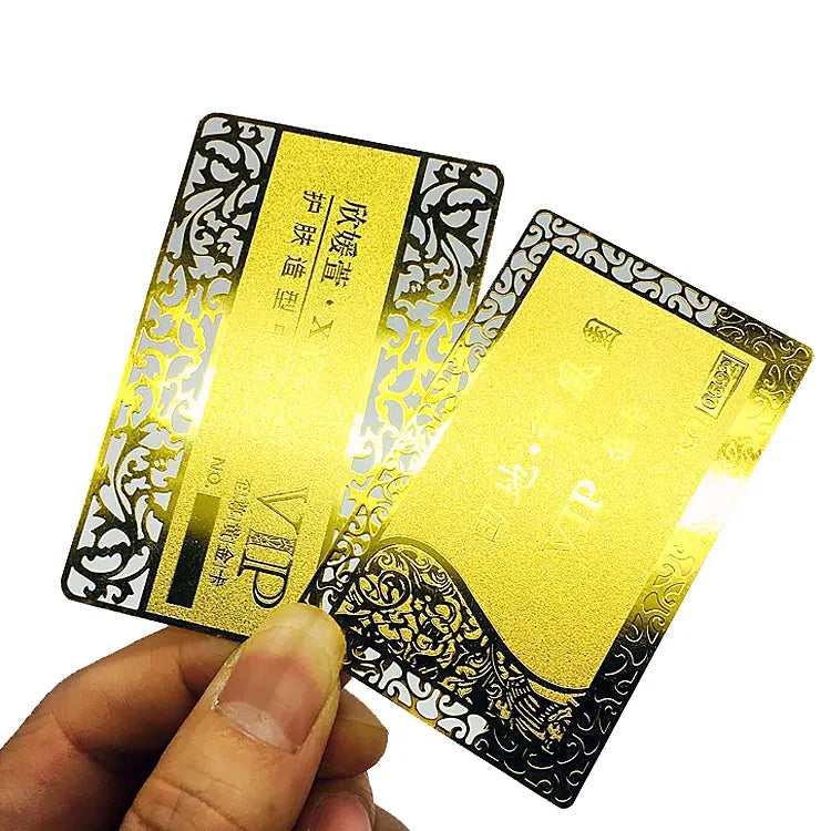 Gold-tone metal business cards with black lettering and decorative edge patterns