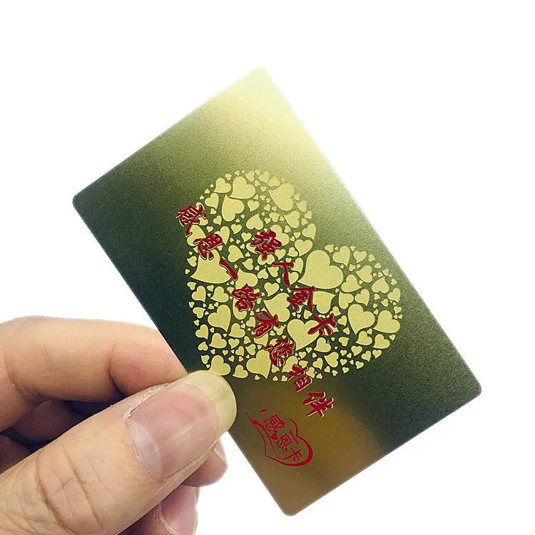 Hand holding a gold-tone metal card with a red tree design and decorative perforations