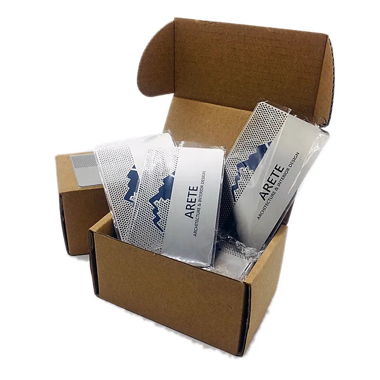 Printed silver-tone metal business cards in protective sleeves standing inside an open cardboard box