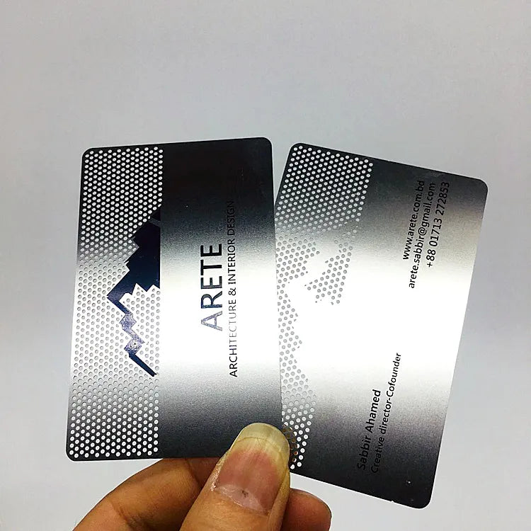 Hand holding silver-tone metal business cards with dark mountain logos and printed contact information