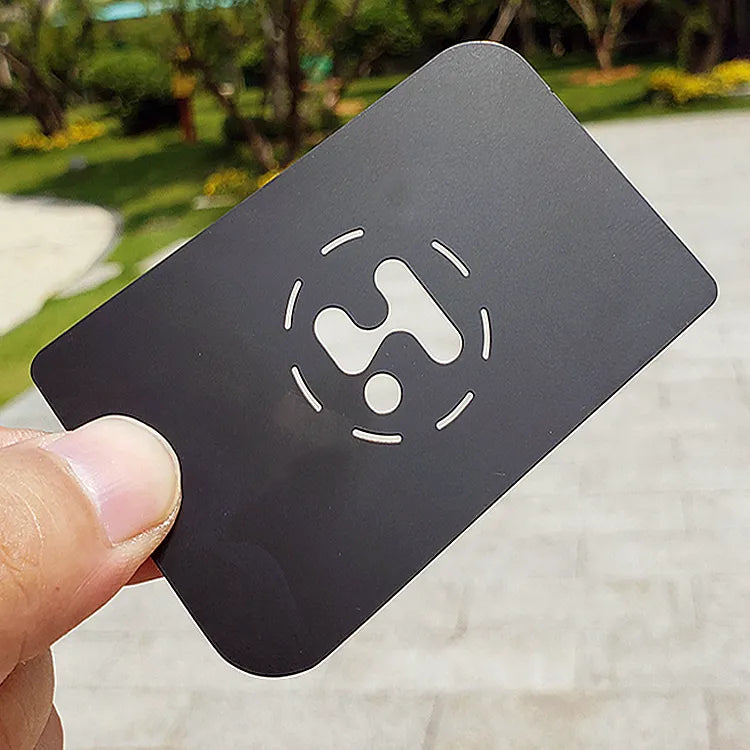 Black metal business card with a large light-colored symbol held outdoors