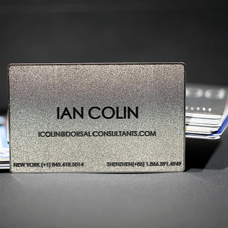 Silver-tone metal business card with IAN COLIN lettering on a dark background
