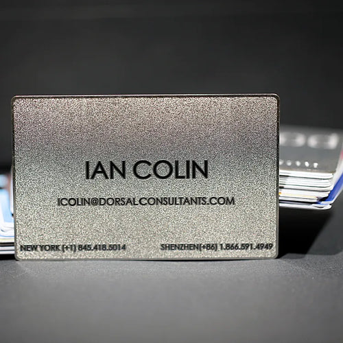 Silver-tone metal business card with IAN COLIN lettering on a dark background