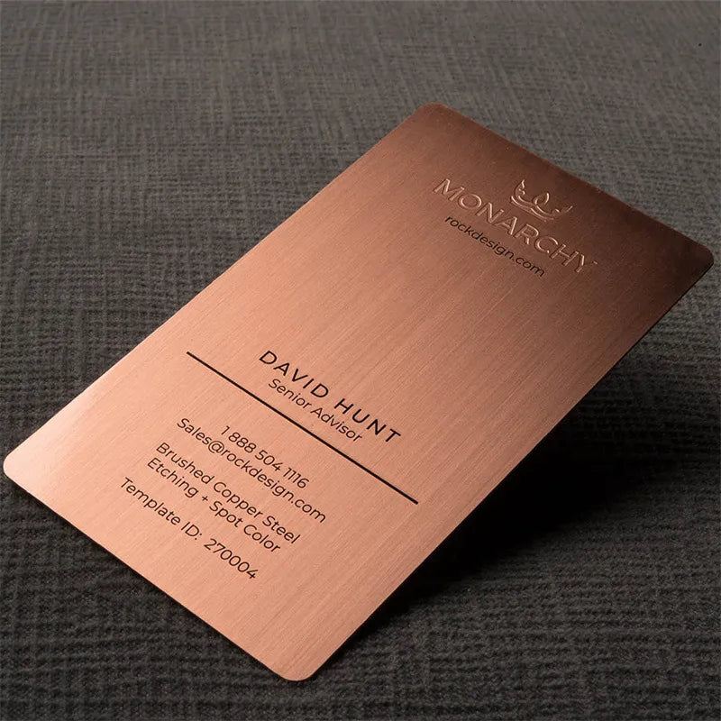 Copper-tone metal business card with fine contact lettering on a dark surface