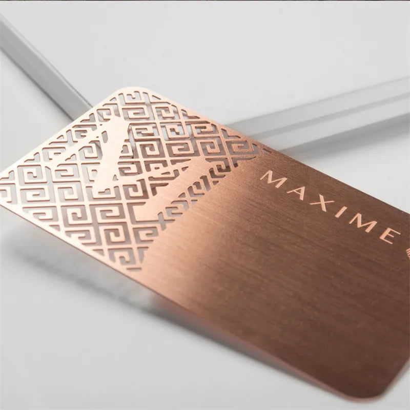 Rose-gold-tone metal business card with an intricate geometric cutout pattern and fine lettering