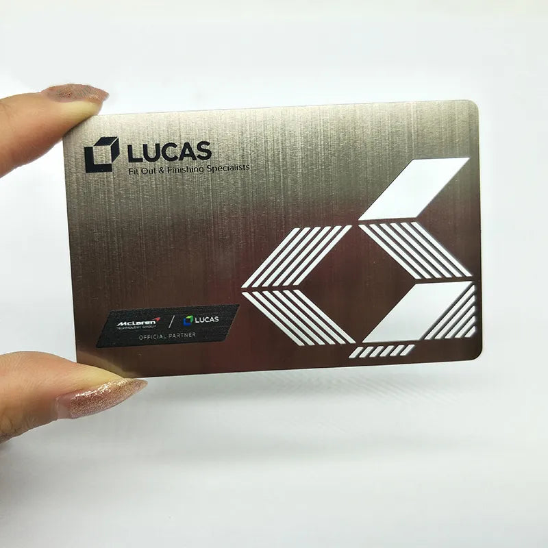 Reflective gold-tone metal business card with LUCAS lettering and a geometric light-colored logo