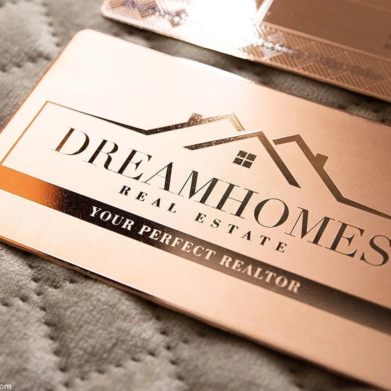 Rose-gold-tone metal business card with DREAM HOMES lettering and a house logo