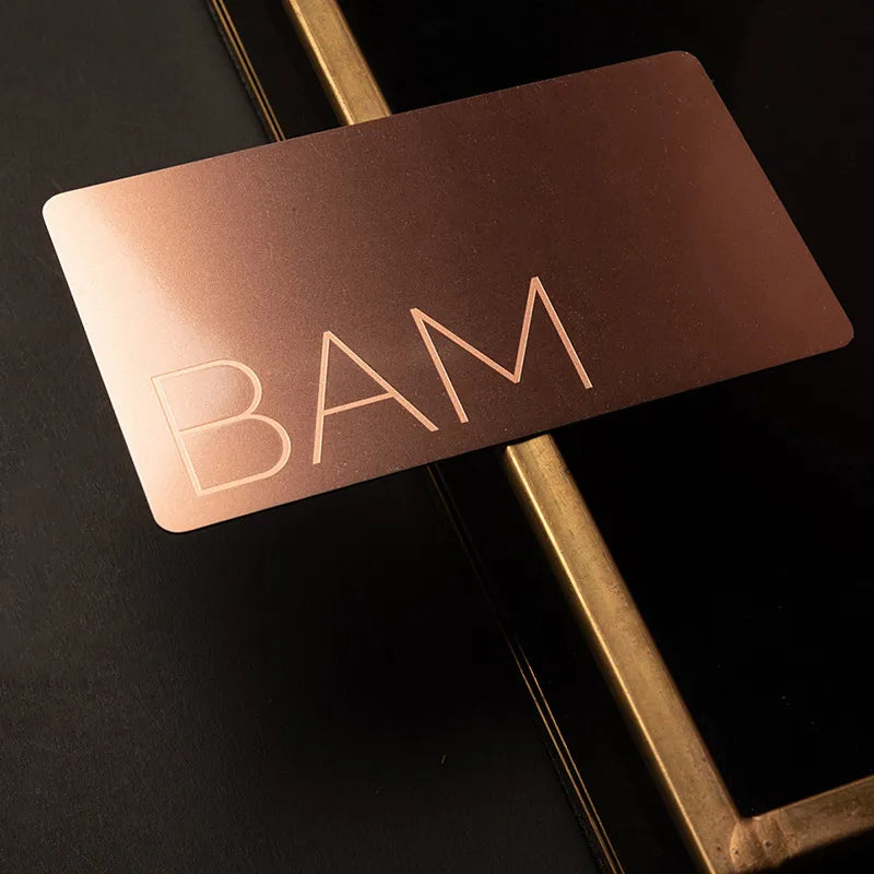Copper-tone metal business card with SAM lettering displayed on a narrow stand