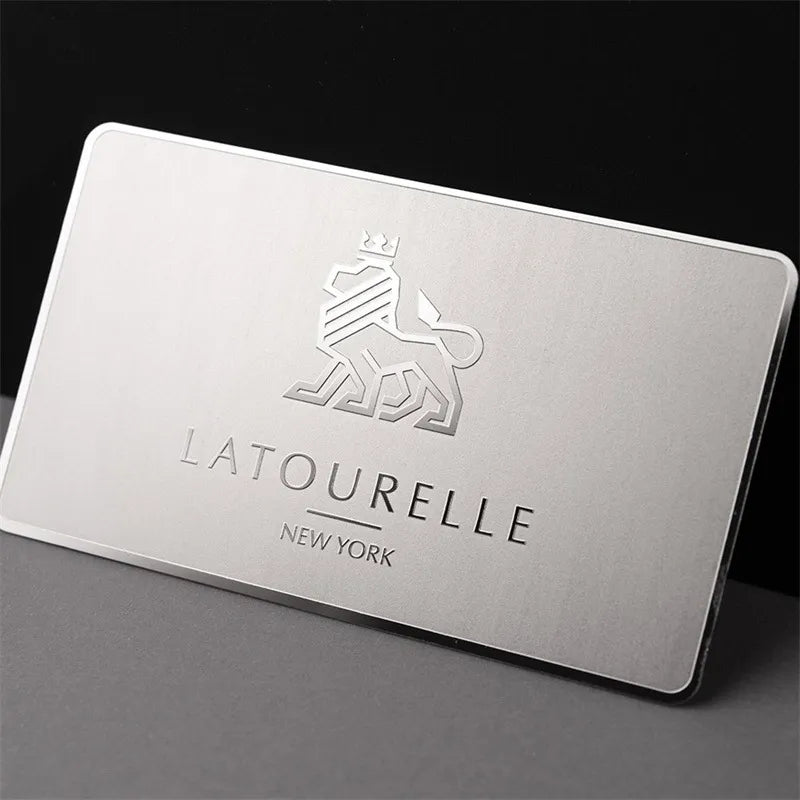 Silver-tone metal business card with LA TOURELLE lettering displayed on a dark background