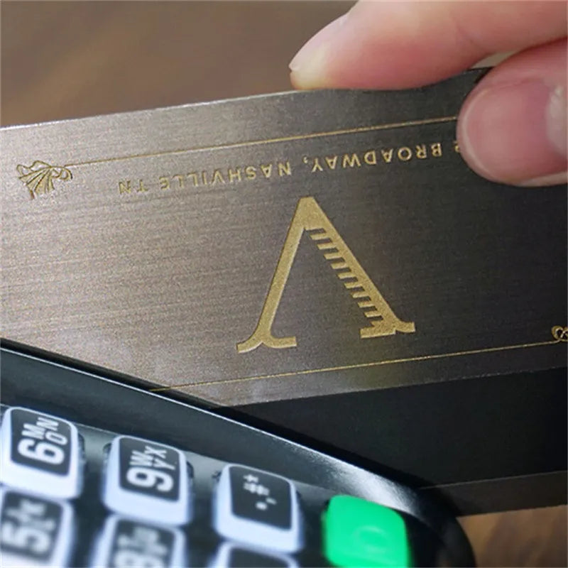 Dark metal business card with a gold-tone triangular logo and fine horizontal artwork
