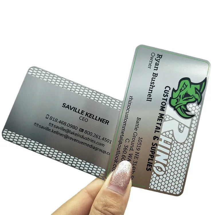 Two silver-tone metal business cards with perforated patterns and printed contact details held in one hand