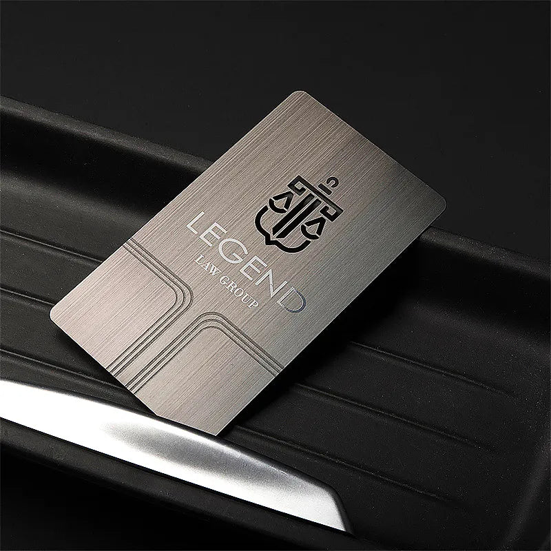 Silver-tone metal card with a dark calligraphic logo resting on a dark ridged surface