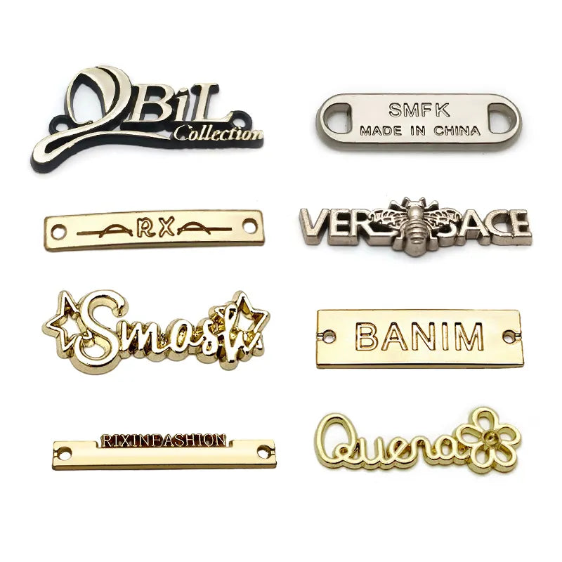 Assortment of custom metal clothing tags showcasing diverse cutout silhouettes, cursive lettering, and polished finishes