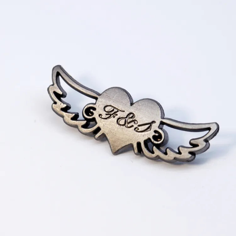 Gunmetal winged heart metal logo badge with cursive engraved monogram lettering