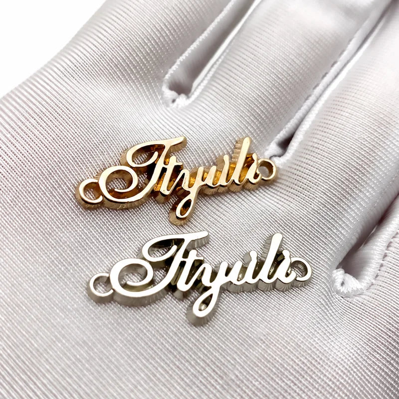Custom cursive metal clothing labels in polished gold and silver finishes with attachment holes