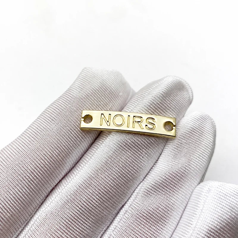 Polished stainless steel rectangular clothing tag plate held in gloved hand