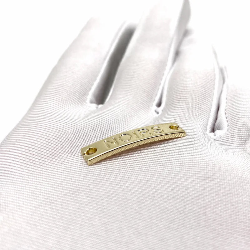 Assorted custom metal tags for clothing in gold, silver, and black enamel finishes