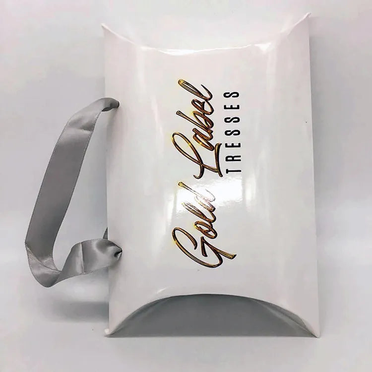 White pillow-shaped paper gift bag with gray ribbon handles and gold-colored lettering