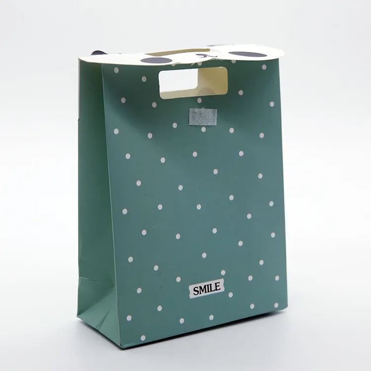 Green paper gift bag with a die-cut handle and small decorative white motifs