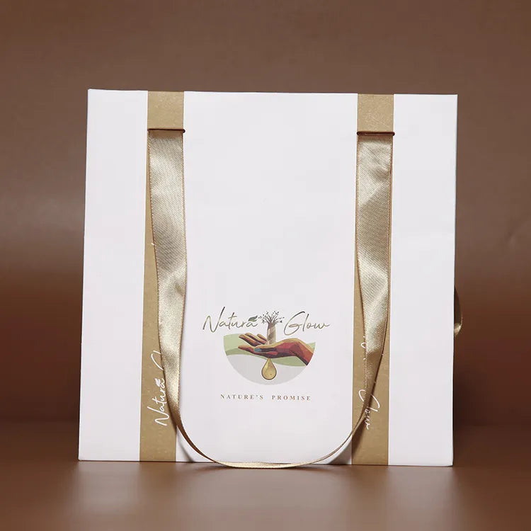 White paper carrier bag with gold-colored ribbon handles and a centered printed logo