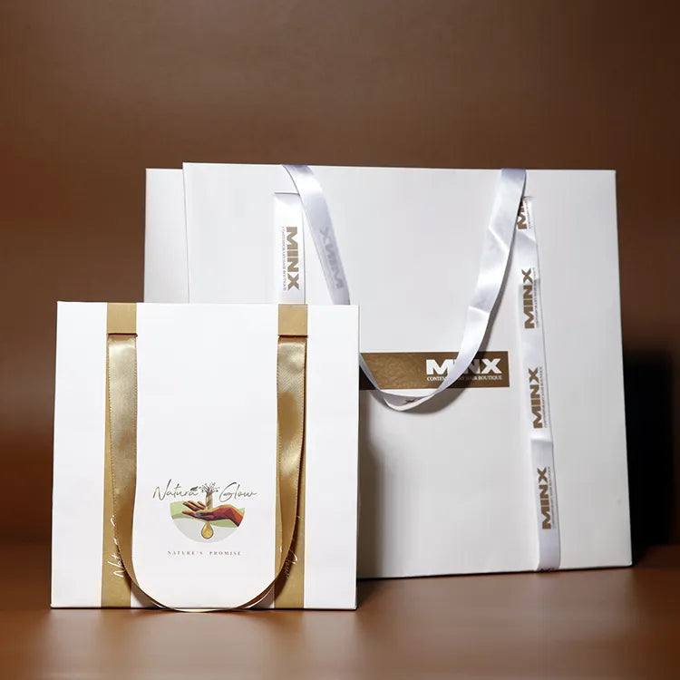 White paper shopping bags with gold-colored ribbon handles and a printed logo