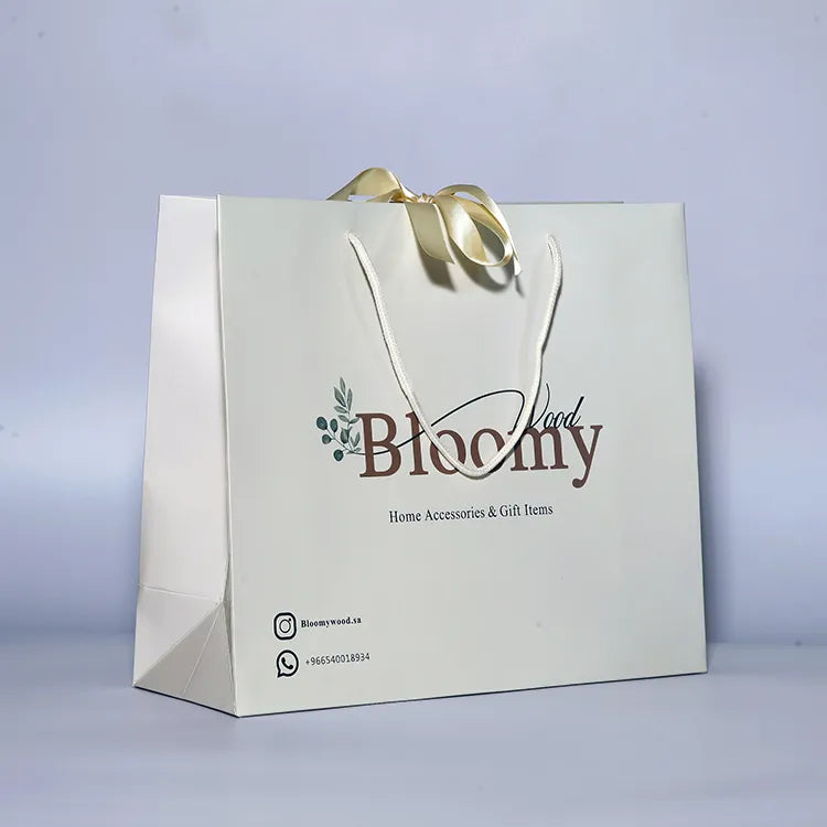 White paper gift bag with gold-colored cord handles and a printed floral logo