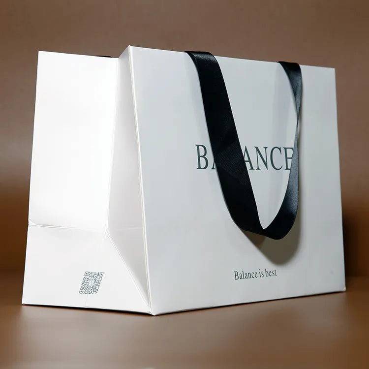 White paper shopping bag with wide black ribbon handles shown at an angle