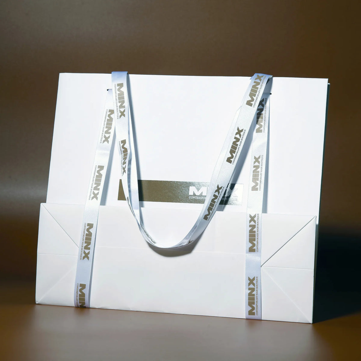 White paper shopping bag with wide dark ribbon handles and printed lettering