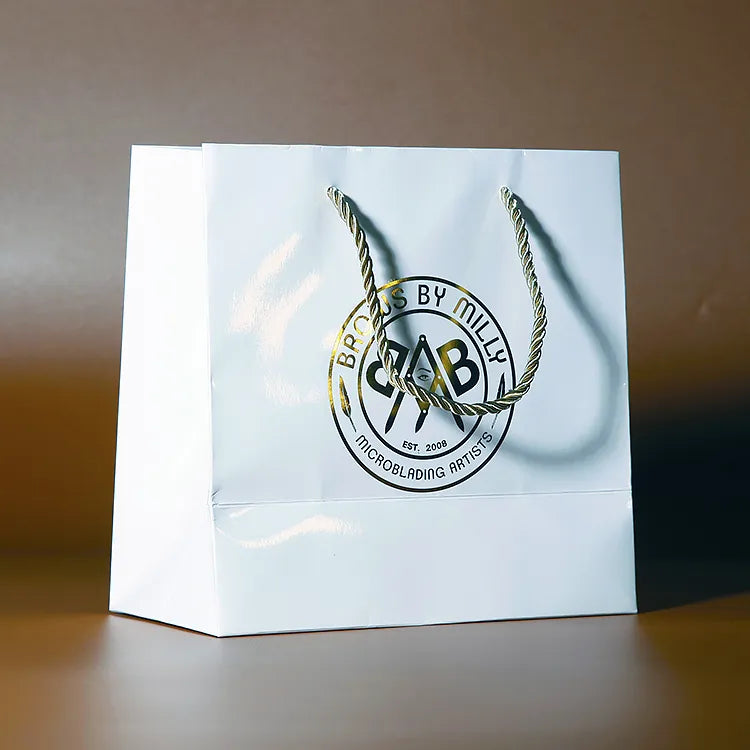 White paper shopping bag with green cord handles and a decorative green emblem