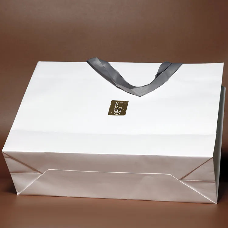 White paper shopping bag lying flat with contrasting dark handles and a small label