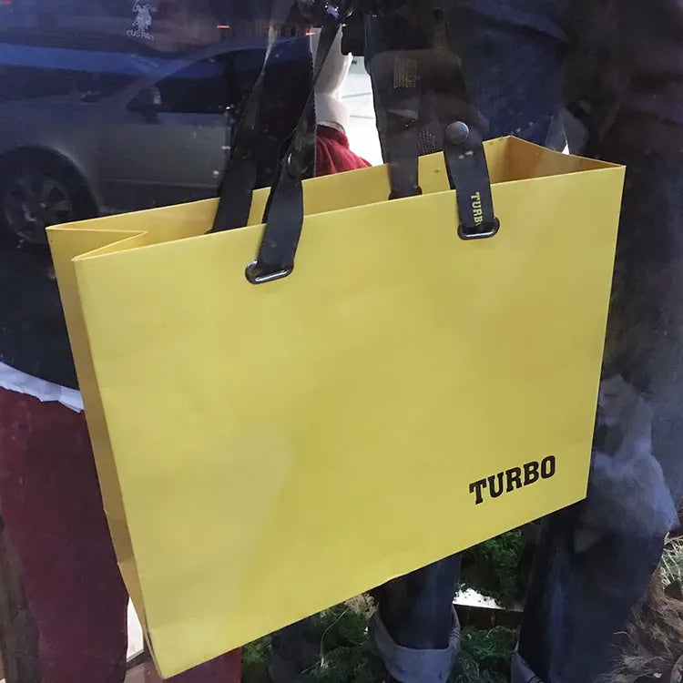 Yellow paper carrier bag with contrasting dark handles held in a retail display
