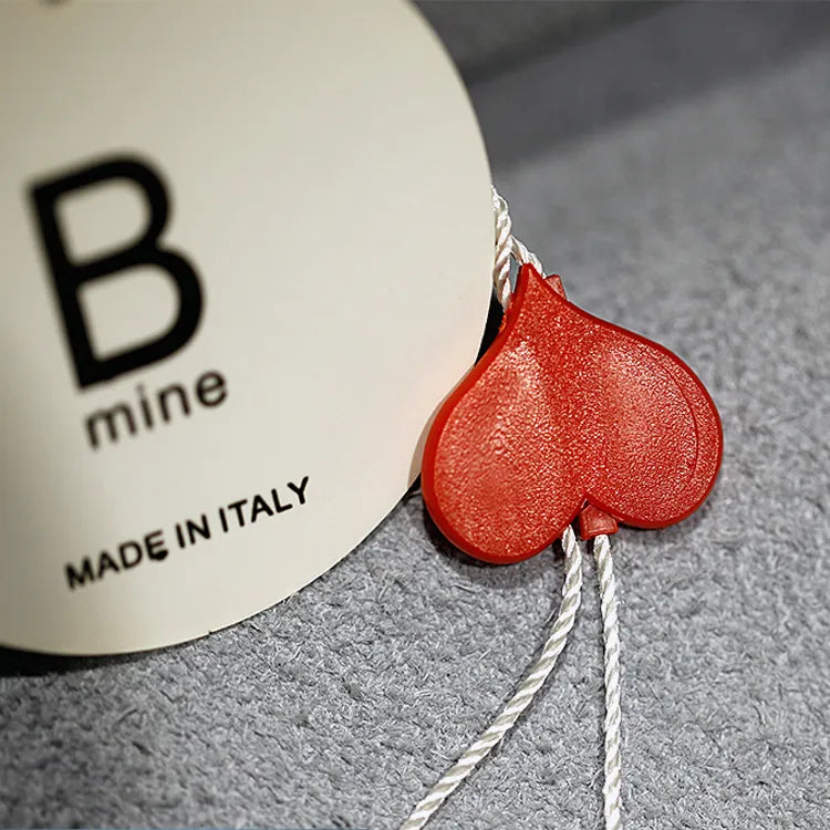 White round hang tag with black lettering, white cord and red heart-shaped seal