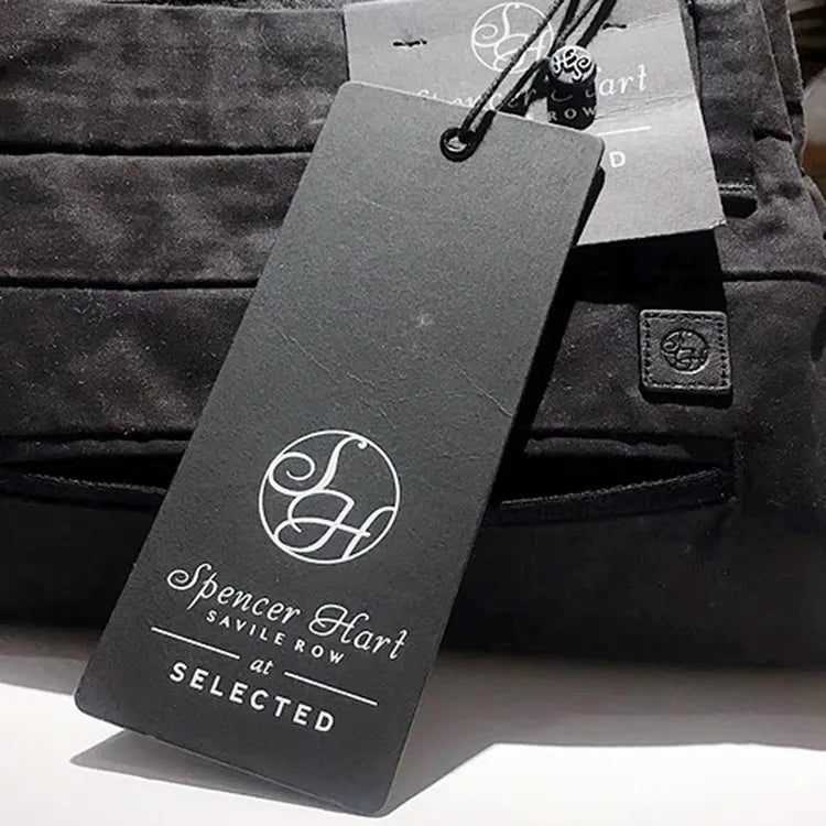 Long grey printed clothing hang tag with white monogram and black string attached to trousers